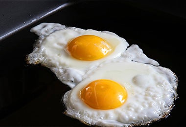 Dos huevos fritos en una parrilla con una superficie negra para preparar huevos shakshuka.