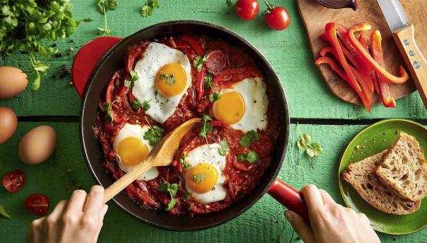 Huevos shakshuka con hierbas, salsa de tomate, pan y pimentón picado en toma cenital.