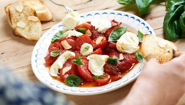 Ensalada caprese con tomate, queso, albahaca y pan en un plato.